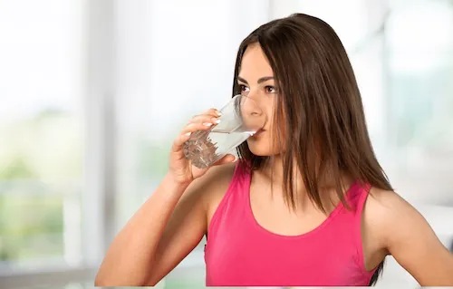 Femme boit de l'eau, intérieur lumineux.