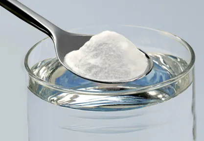 Cuillère à café de bicarbonate de soude au-dessus d'un verre d'eau tiède, pour préparer un bain de bouche contre les aphtes.