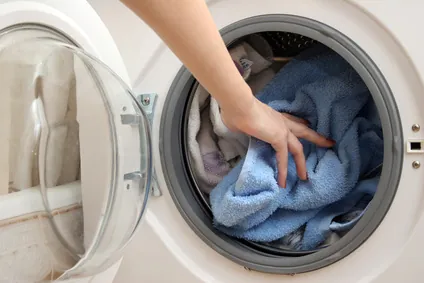 Main ajoutant linge dans machine à laver.